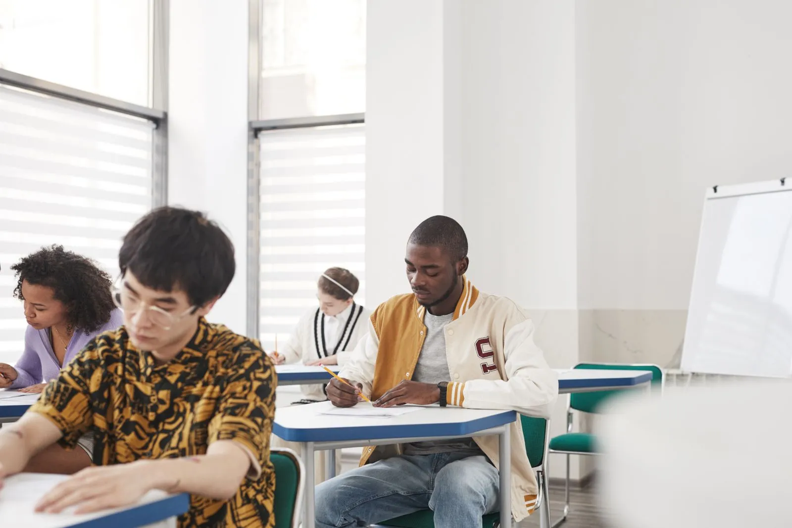 Jovens concentrados fazendo prova nas carteiras de uma sala de aula