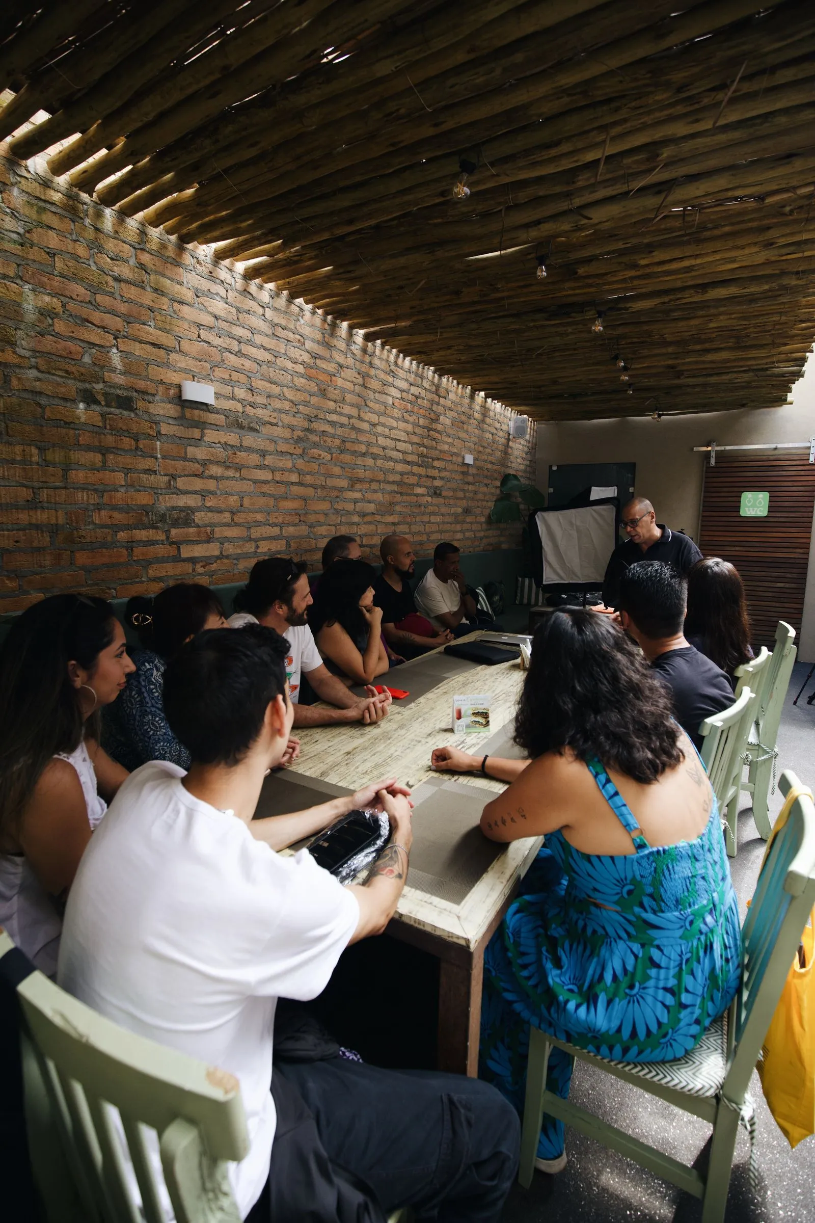 Grupo de adultos sentados em volta de uma mesa comprida ouvindo o instrutor em um workshop